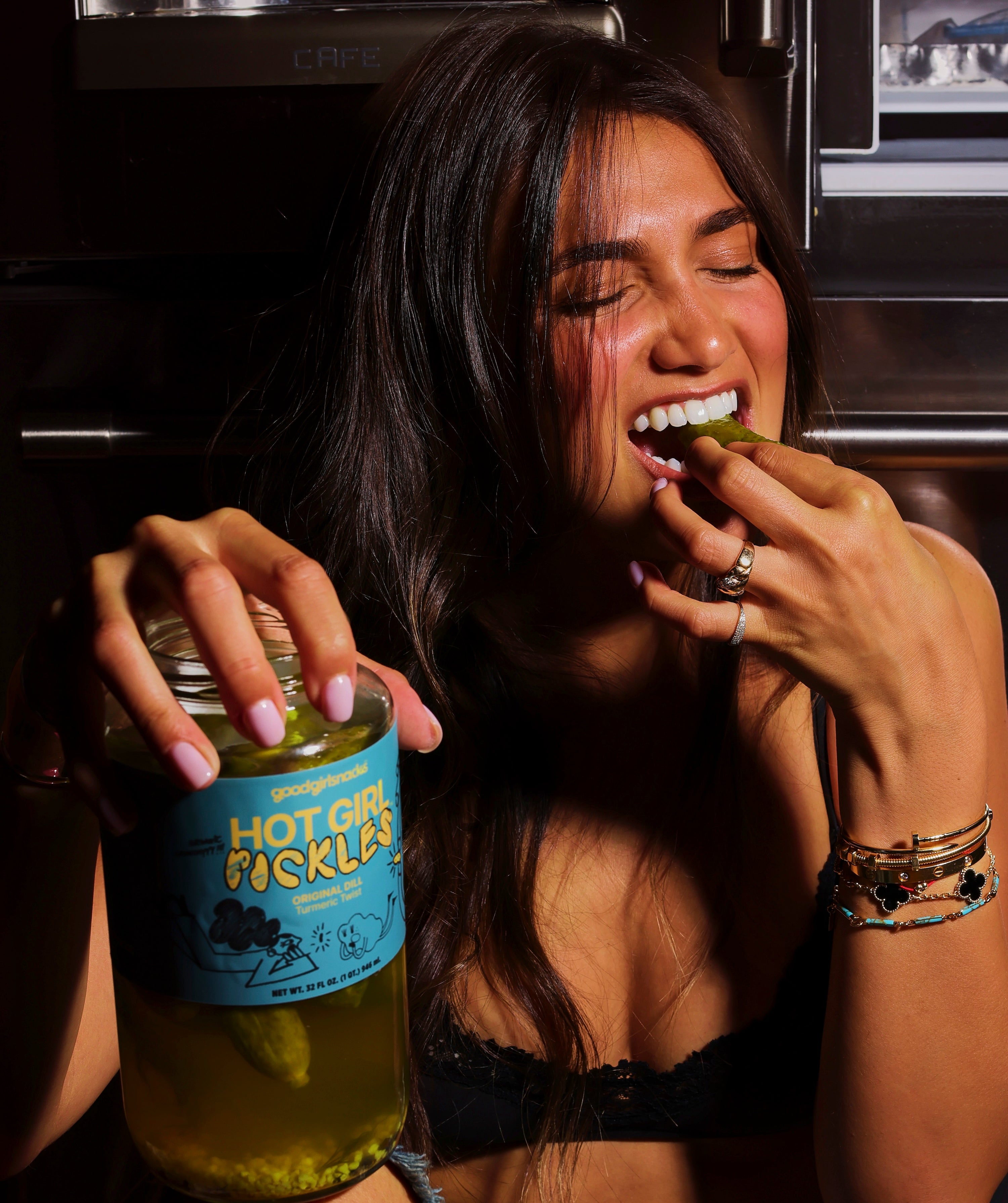 A model bites into a Hot Girl Pickle while holding the jar in her other hand.